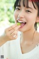 A woman eating a piece of fruit with her mouth open.