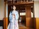 A woman in a blue hanbok standing in front of a door.