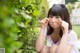 A young woman sitting on the ground in front of a bush.